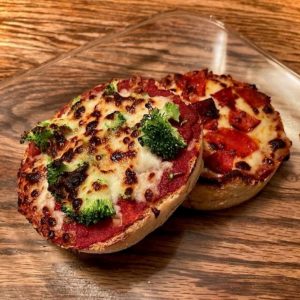 Photo of two miniature pizzas, one topped with broccoli and the other topped with pepperoni, on a clear glass plate on a wooden table.